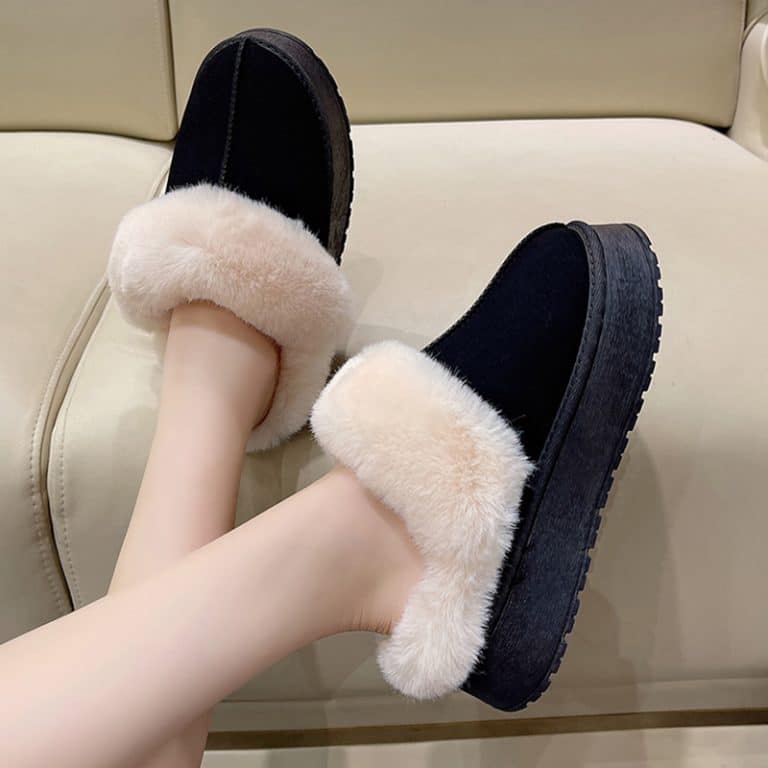 Female feet wearing black orthopaedic slippers with a fluffy interior on a couch.