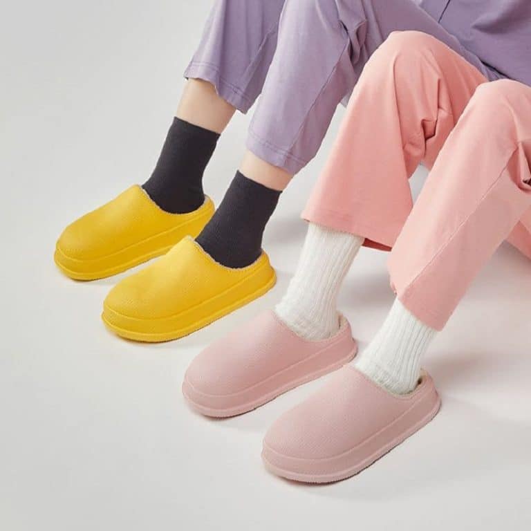 Assorted yellow and pink slippers worn with socks on a gray floor.