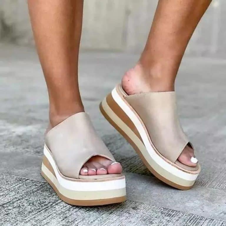 Orthopedic slides for women in beige leather, with thick striped sole, worn in an urban setting.