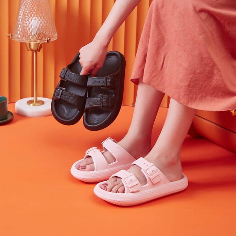 Two pairs of orthopedic sandals, one in pink and the other in black, worn on an orange background.