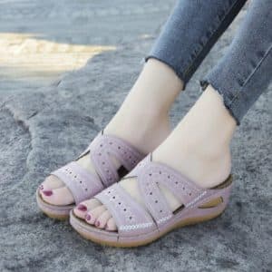 Mules in leather for women, lavender color, with perforations and floral patterns, on a rocky ground.