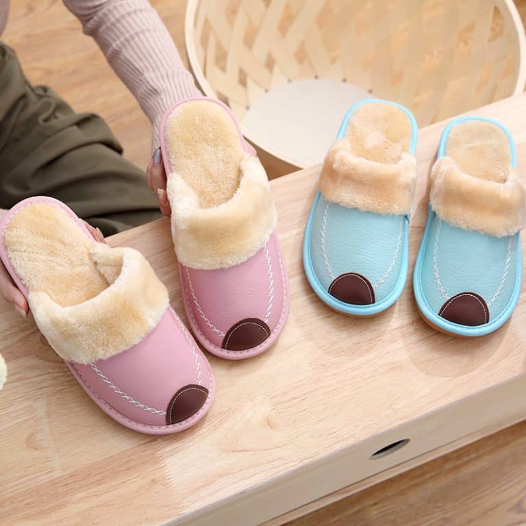 Pair of pink and sky blue leather slippers on a wooden piece of furniture.