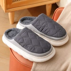 Slippers for men in grey and navy blue, quilted design with grey fur lining and white sole.