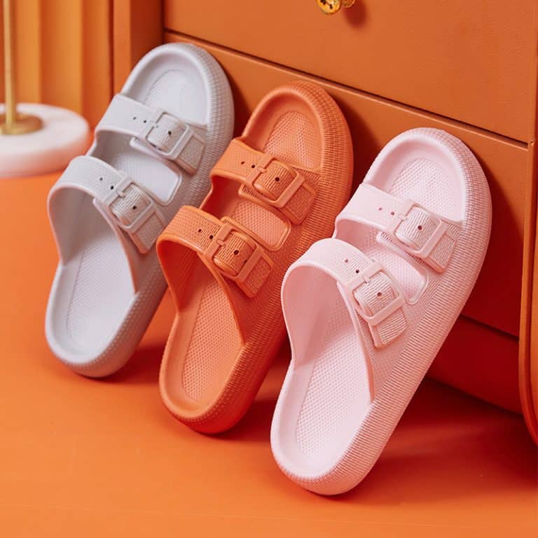 Three pairs of women's orthopedic buckle sandals in pink, orange, and white lined up on an orange background.