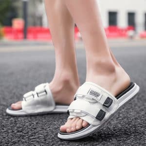 Profile view of black Velcro slides with adjustable straps on a sidewalk.